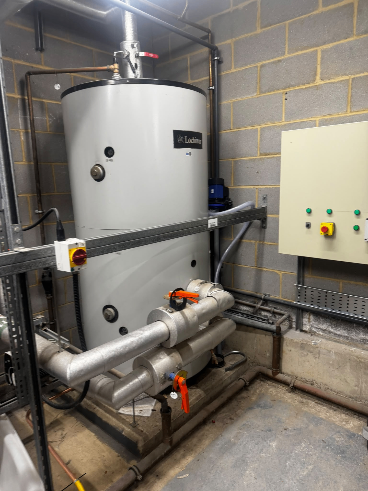 Large commercial calorifier installation in a plant room with insulated pipework and control panel